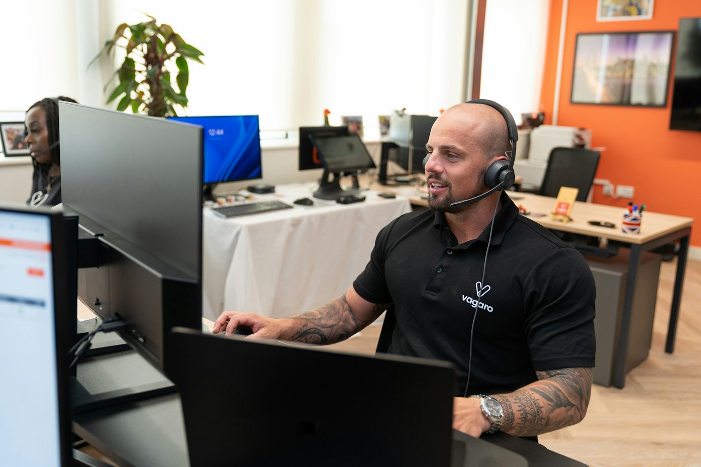 Mann mit Bart und Tattoos am Headset, der an Computermonitoren arbeitet.