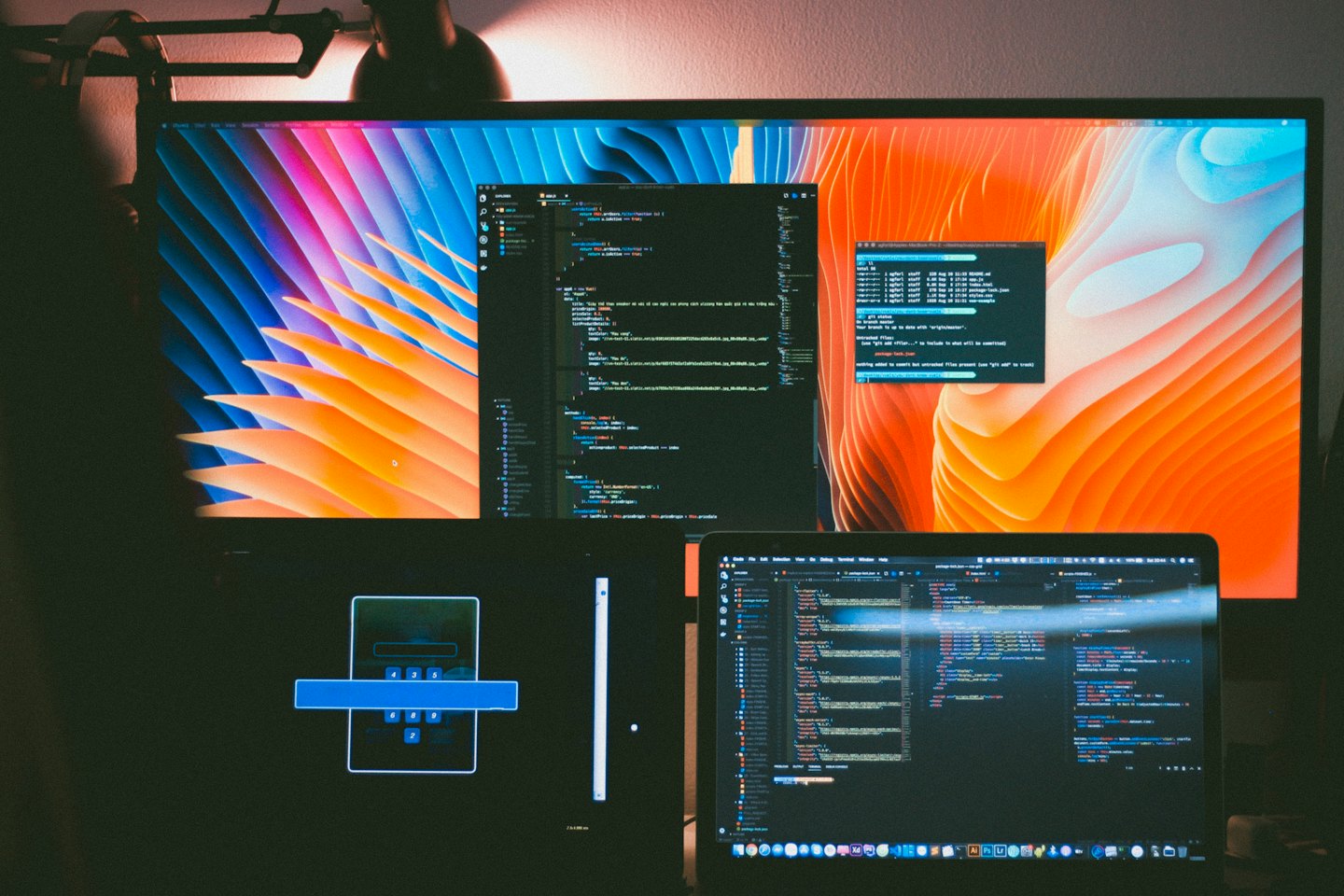 Bildschirme eines Entwicklers mit buntem Code und abstrakten Wellen bei Nacht.
